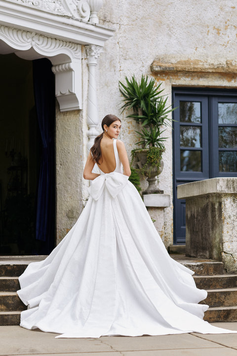 Allison Webb Wellsley Wedding Dress - a floral jacquard A-line gown with pleats, a plunging V-neck, low scoop back, pearl detail and a detachable bow.